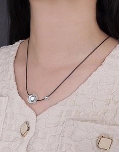 Detail of silver dual bead pendant on black cord worn with elegant cream tweed jacket