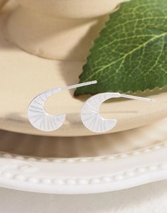 Macro shot of silver crescent moon earrings with radiant texture on a ceramic tray
