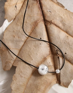 Detail of S925 silver ball pendant on black cord over natural autumn leaves