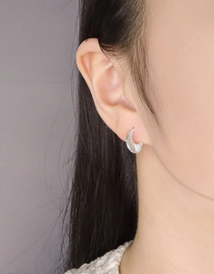 Macro detail of crescent moon earring with textured silver finish on female ear