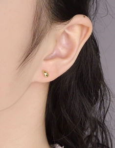 Gros plan d'une puce d'oreille goutte dorée minimaliste à la finition polie sur modèle