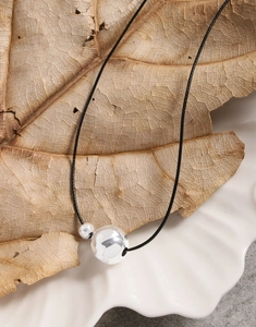 Minimalist S925 silver spheres on black cord shown over aesthetic leaf and ceramic plate