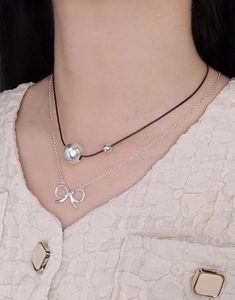 Close-up of S925 sterling silver ball necklace layered with a delicate bow pendant