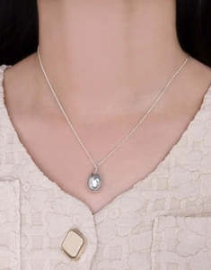 Detail of silver S925 teardrop necklace worn on a textured beige sweater for women