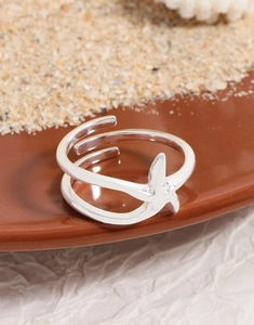 Detailed view of silver starfish open ring on sand and coral beach themed background