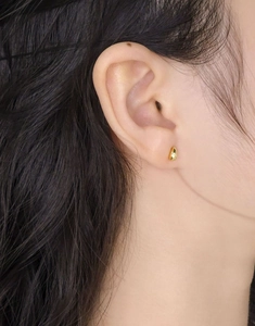Gros plan d'une boucle d'oreille goutte en or poli portée sur l'oreille de femme
