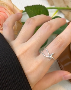 Close-up of a minimalist silver starfish open ring worn on a finger with floral decor