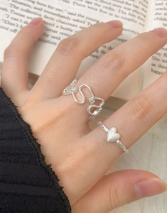 Detail of silver S925 heart ring set and wave band with zircon on hands over a book