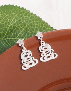 Macro shot of silver Christmas tree earrings with sparkling zircon stars on ceramic plate