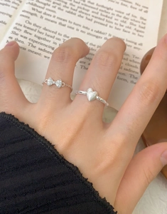 Detailed view of matte heart ring and crystal bow chain ring set worn on finger