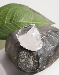 Macro detail of silver wide ring with foil texture on a dark natural stone and green leaf