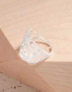 Détail d'une bague argentée ajourée à motif floral vintage sur un support en bois