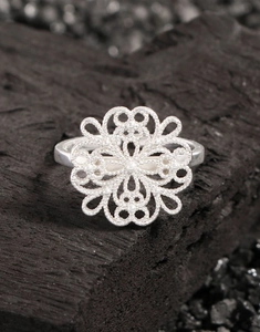 Macro shot of S925 silver hollow floral ring on dark textured charcoal background