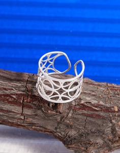 Dettaglio macro di anello a maglie vuote argento con motivi geometrici su corteccia