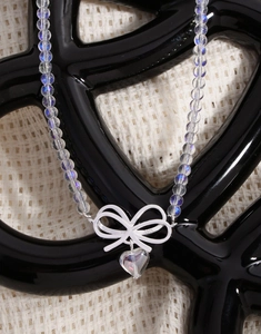 Close-up of S925 sterling silver bow pendant and heart charm on iridescent bead necklace
