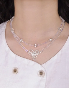 Detail of double-layer beaded necklace with silver bow and transparent heart charms