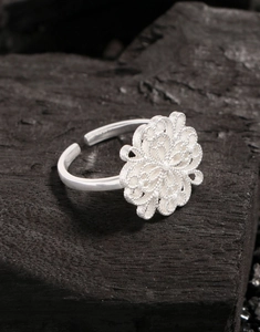 Macro shot of silver hollow floral ring with intricate filigree details on charcoal wood