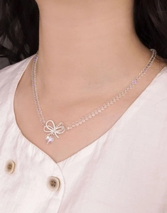 Detail of beaded necklace with silver bow and crystal heart pendant on white shirt