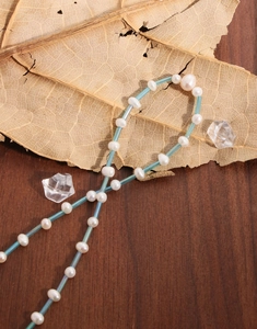 Vue détaillée du collier avec perles naturelles et tubes en verre bleu clair sur bois