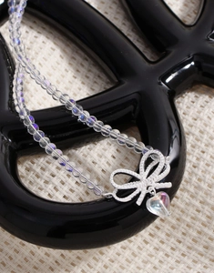 Macro view of crystal bow heart pendant necklace with aurora beads on black stand
