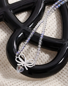 Detail of iridescent beaded necklace with silver bow and heart-shaped crystal pendant
