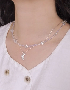 Detail of layered S925 silver necklace with heart beads and croissant pendant on model