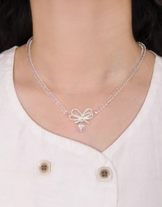 Detailed view of beaded necklace with silver bow and crystal heart pendant on skin