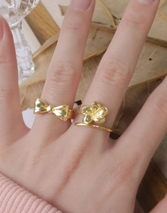 Detail of gold flower and bow rings on finger with pink knit sleeve and warm aesthetic