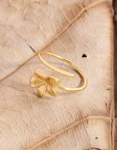 Detailed close-up of a gold-plated flower ring on a natural dried leaf background