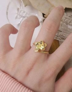 Detail of a 3D gold-plated five-petal flower ring worn by a model in soft lighting