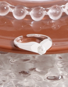 Detail of silver heart-shaped open ring featuring a lustrous white pearl on a ceramic tray