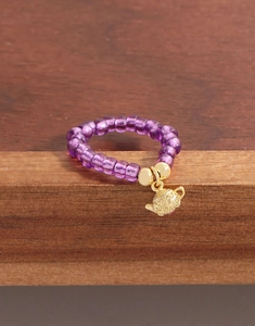 Gros plan d'une bague perlée violette avec un pendentif détaillé en forme de théière dorée