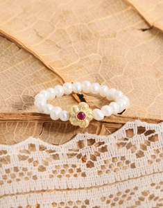 Vue détaillée d'une bague en perles avec une fleur dorée et une gemme rouge au centre