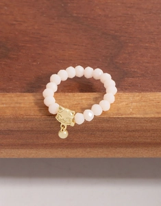Détail d'une bague élastique en perles roses avec pendentif chat doré sur bois