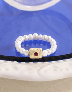 Macro shot of S925 silver ring with freshwater pearls and red gemstone on a porcelain plate