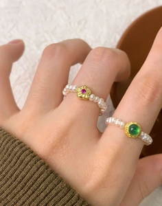 Détail de bagues en perles d'eau douce avec fleur dorée et pierre verte sertie