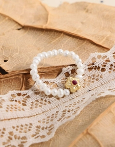 Gros plan de la bague en perles avec fleur et pierre rouge sur dentelle vintage