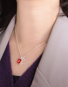 Detail of S925 silver necklace with red zircon stone and key pendant on a model