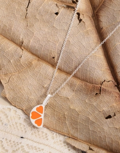 Close-up of S925 silver necklace featuring orange enamel heart pendant on a lace leaf background
