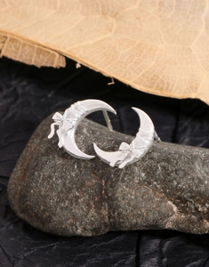 Macro shot of silver crescent moon earrings with bow detail on a textured dark rock