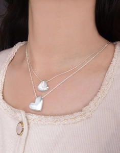 Detail of layered S925 silver necklaces featuring a matte brushed heart and shell pendant