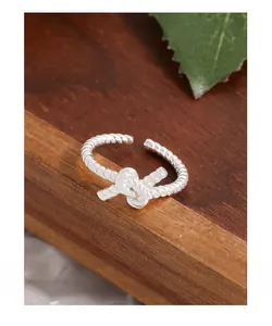 Macro shot of silver S925 twisted knot ring on wooden base with green leaf detail