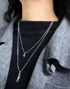 Detail of layered S925 silver necklace with star and twist knot pendants on a model