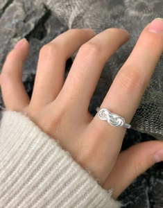 Detail of silver S925 multi-layer cross winding knot ring on finger with white sweater