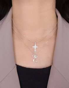 Close-up of layered silver S925 cross and bow pendants with zircon pavé for women