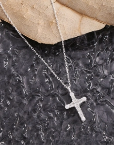 Detailed close-up of a silver cross necklace with clear zircon stones on a leaf