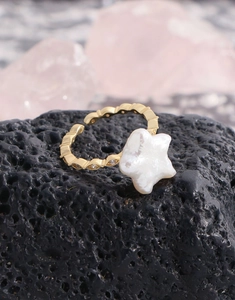 Vue macro d'une bague étoile en perle dorée avec texture losange sur roche volcanique