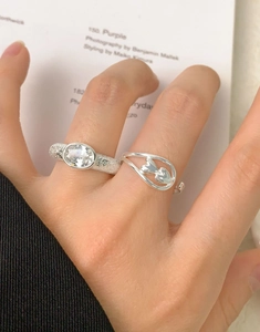 Detail of silver rings with oval zircon and heart design worn on hand against paper