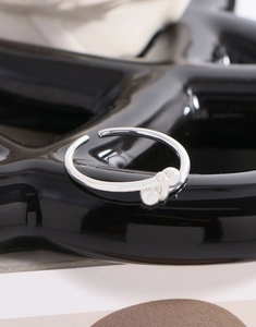 Vista macro di un anello aperto in argento con perline minimaliste su superficie nera