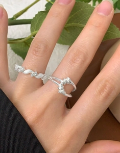 Détail d'une bague argentée torsadée et d'un anneau ondulé serti de zircons sur le doigt
